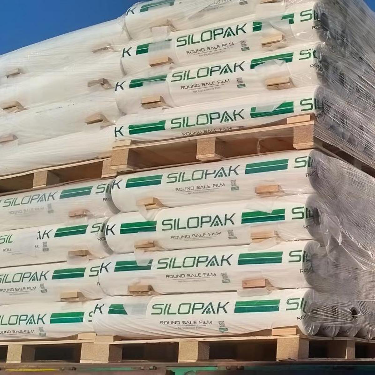 Silopak round bale film rolls stacked on pallets under clear sky, ready for delivery